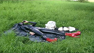 Fetish slave in latex walks and sucks a dildo on the grass